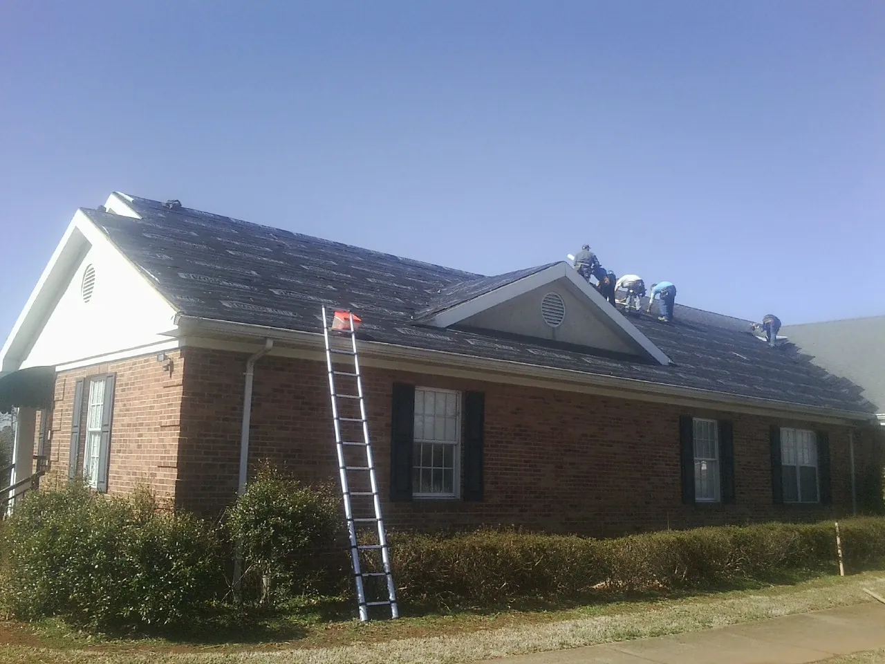 Crew tearing shingles off a brick ranch roof with a ladder set — Emergency Roof Repair work by our crew in Sherman Oaks