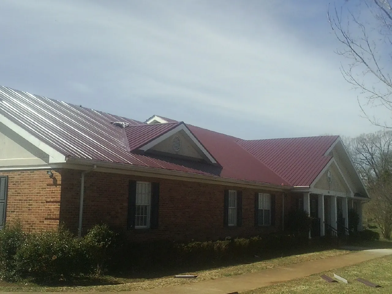 Red metal roof with gabled entries on a long brick building, from a Hail Damage Roof Repair job in Sherman Oaks