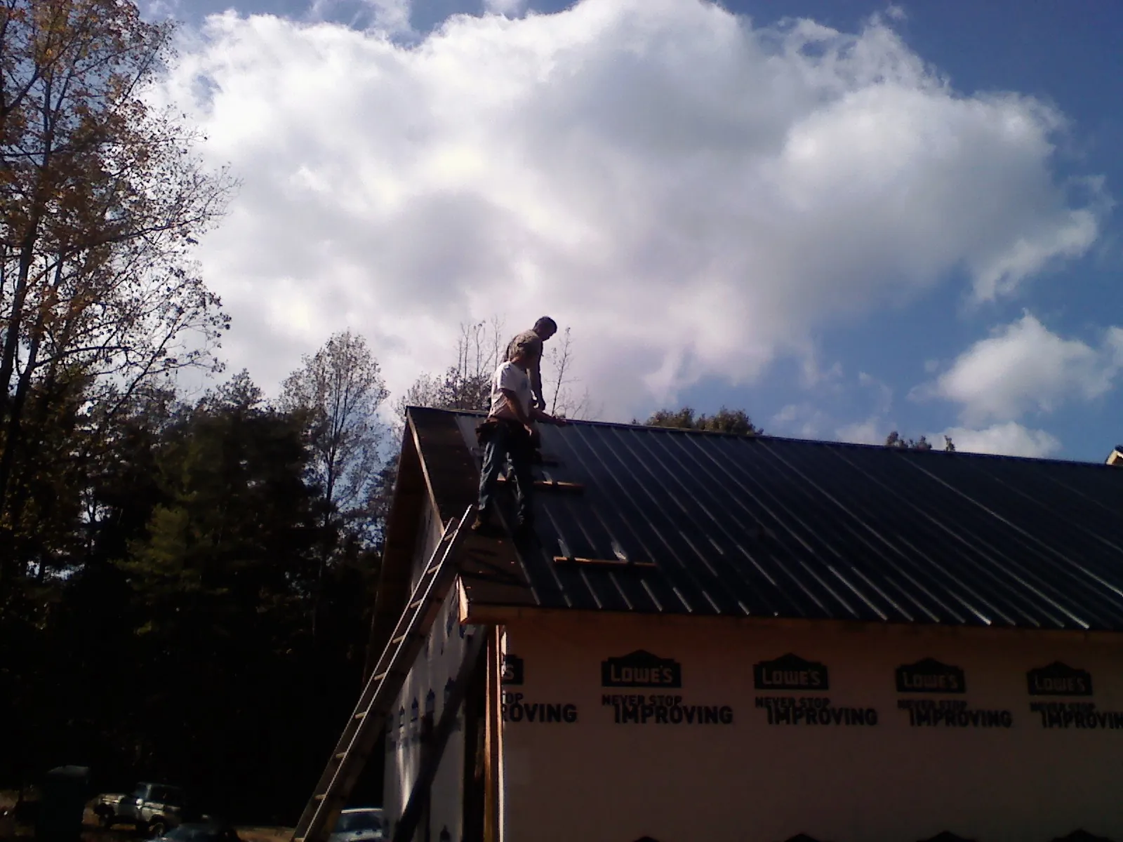 Roofer fastening dark metal panels high against a cloudy sky, from a Roof Inspection job in Sherman Oaks