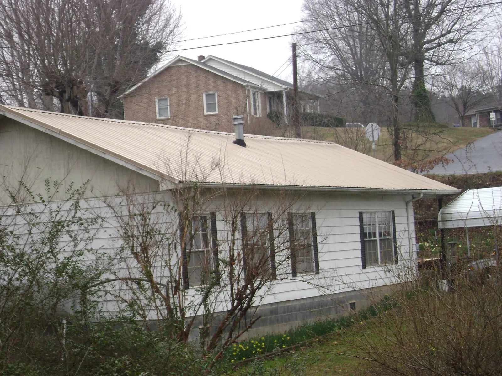 Tan metal roof on a white sided house set into a hillside — Commercial Roofing by Roofing Brothers in Sherman Oaks